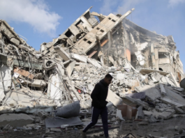 A Palestinian man walks past the remains of a tower which was destroyed by Israeli air strikes in Gaza City
