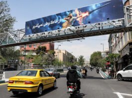 A banner depicting the mythical Persian hero Arash the archer firing a missile from his bow, with text in Persian reading 'I will not abandon my homeland,' hangs on a suspended pedestrian bridge crossing in central Tehran on April 15, 2024. (Atta Kenare/AFP)