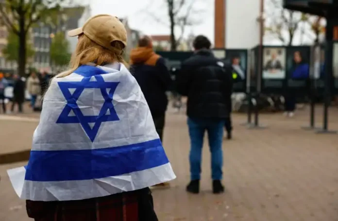 A woman wrapped in an Israel flag stands outside the place where mayor of Amsterdam Femke Halsema attends a press conference following the violence targeting fans of an Israeli soccer team, in Amsterdam, Netherlands, November 8, 2024. (photo credit: PIROSCHKA VAN DE WOUW/REUTERS)