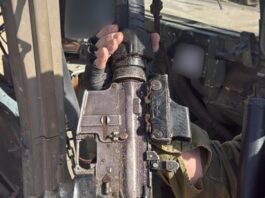 An IDF soldier inspects a recovered weapon and explosive device inside a booby-trapped compound in northern Gaza during operational sweep